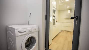 Un lavadero pequeño con lavadora de carga frontal, una kitchenette con microondas y horno, y un puerta corrediza de vidrio que da a un piso de madera.