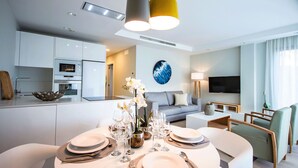 A modern living room with a dining area, a kitchen, and a TV mounted on the wall.