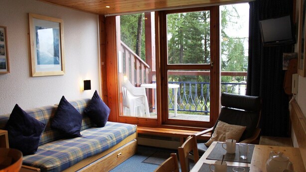 A cozy cabin interior with a sofa, dining table, and a balcony with a railing. - Duplex Apartment in Arc 1800, Aiguille Grive 3, 40m2, ski in/out (Bourg-Saint-Maurice)