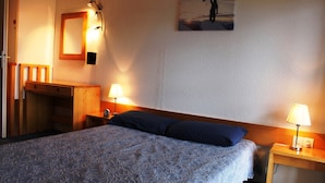A hotel room with a bed, two bedside lamps, a wooden desk, a mirror, and a picture on the wall. - Duplex Apartment in Arc 1800, Aiguille Grive 3, 40m2, ski in/out (Bourg-Saint-Maurice)