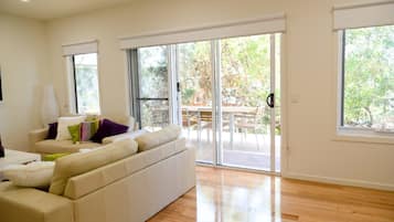 Una sala de estar moderna con un sofá blanco, una lámpara y un ventanal corredero que da a un patio exterior.
