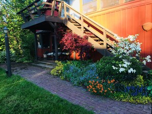 A wooden staircase leading to a porch with outdoor seating, surrounded by a variety of flowering plants and a brick pathway. - BunkHouse Retreat at Minto-Brown Island Salem Oregon  (Salem)