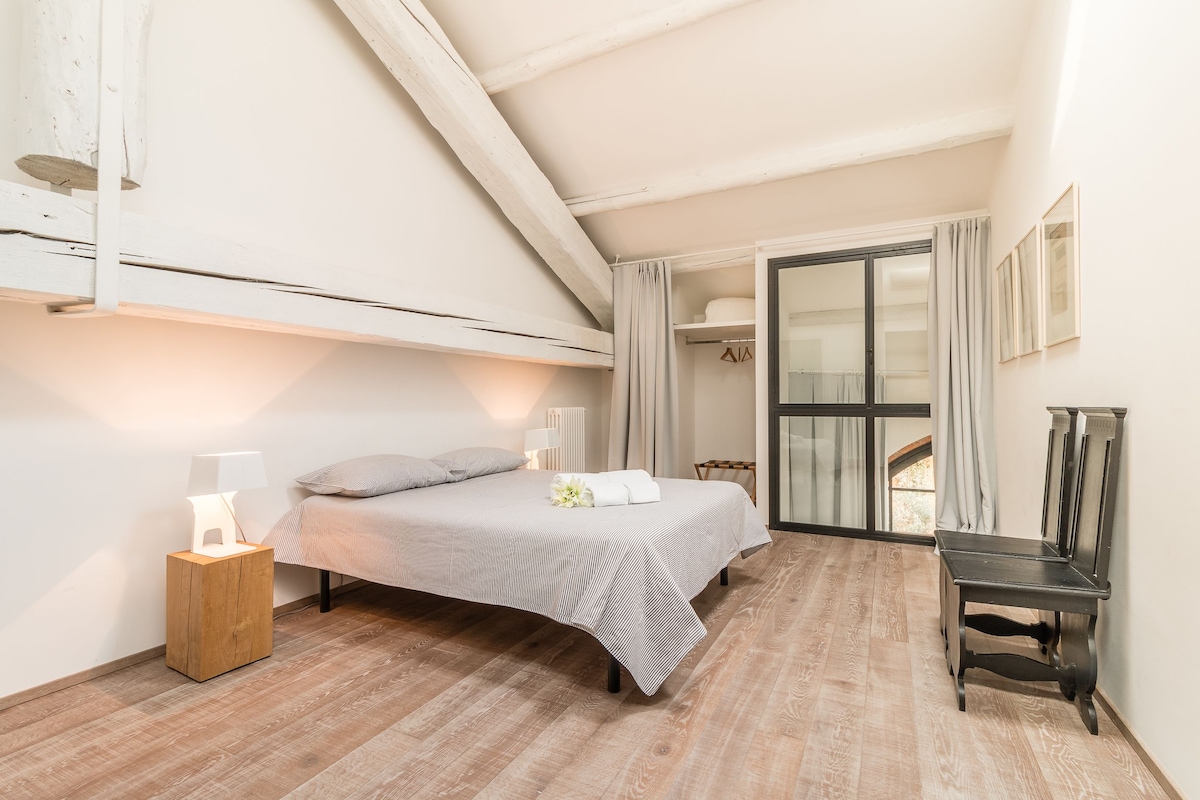 Une chambre à coucher avec un lit, des lampes de chevet, une table de chevet en bois, une chaise et une vue sur un balcon.