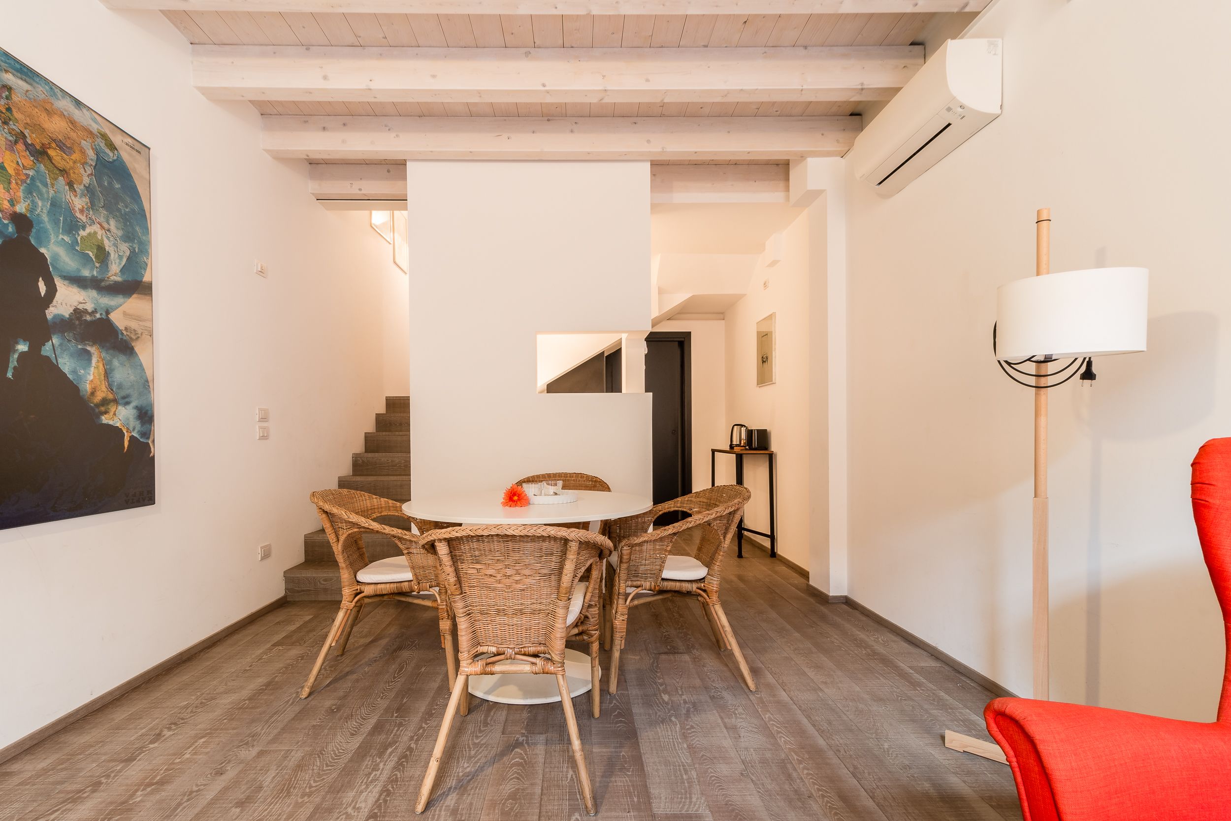 A dining area with wicker chairs and a white table, a red chair, and a floor lamp.