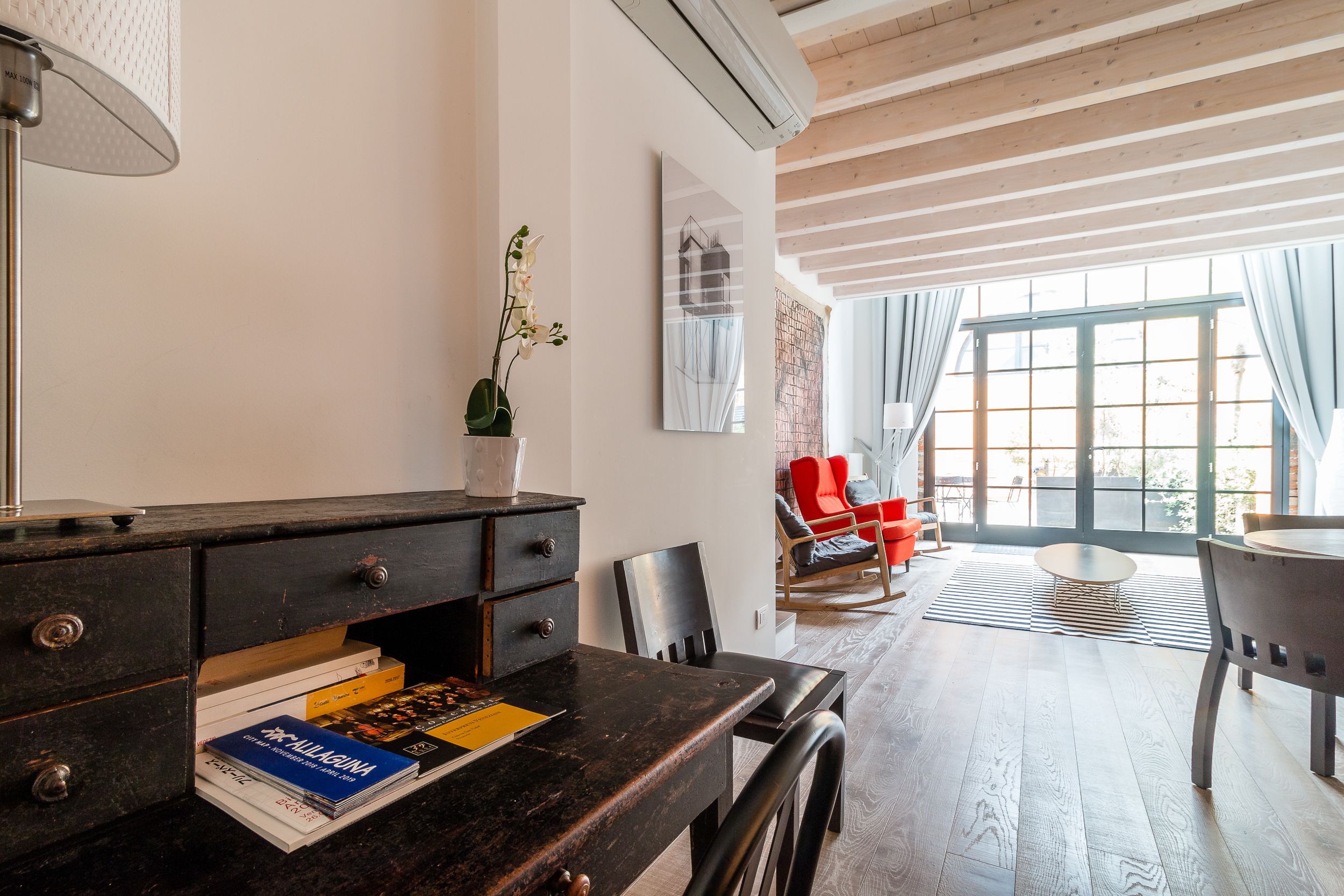 A modern living room with a wooden floor, a dining table, a sofa, and a large window with curtains.