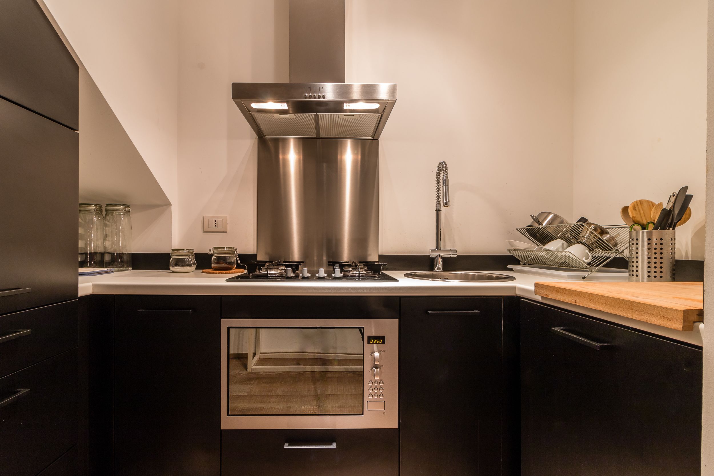 Une cuisine moderne avec des armoires noires, des appareils en acier inoxydable et un plan de travail en bois.