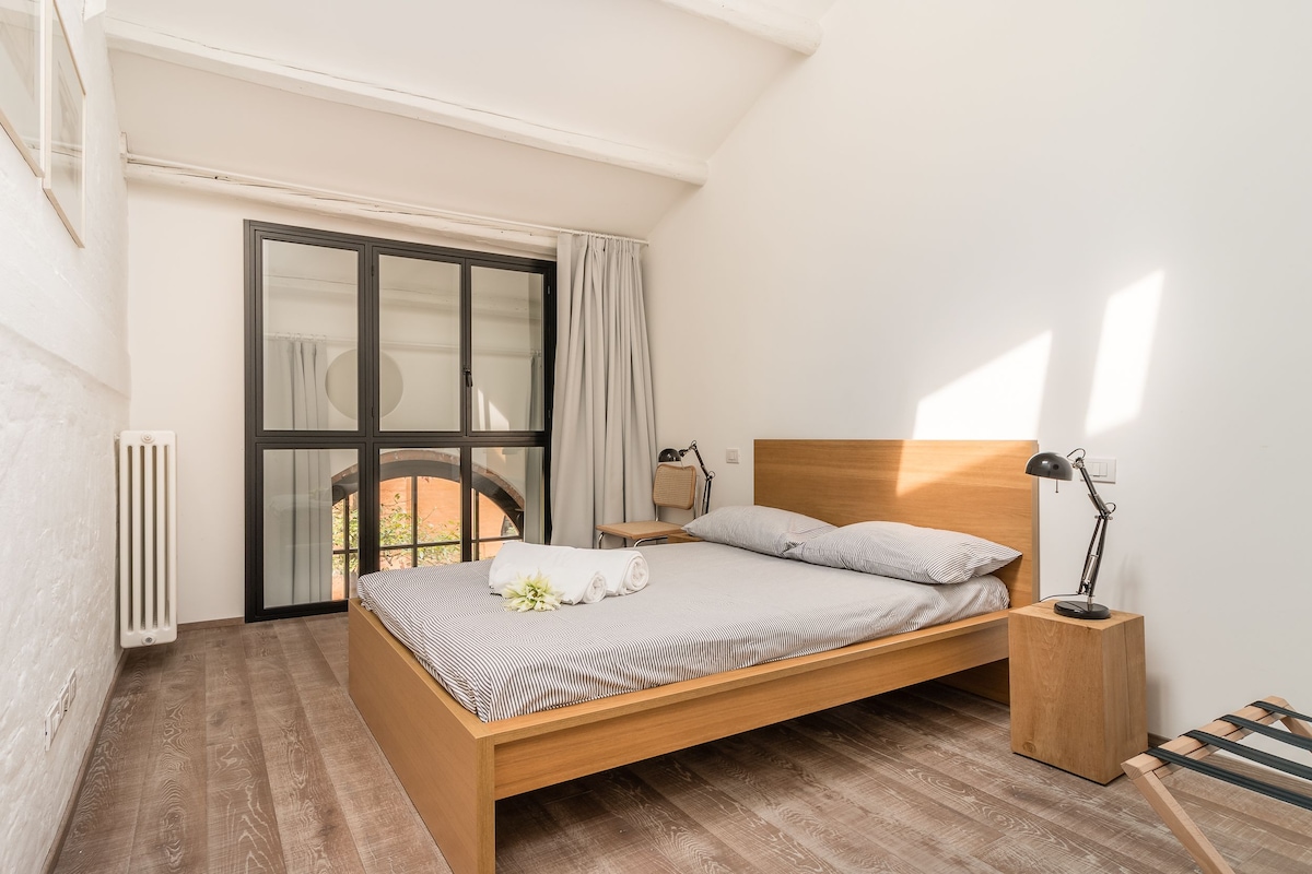 Une chambre à coucher avec un lit en bois, une table de chevet avec une lampe, un radiateur et une fenêtre avec des rideaux.