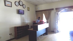 A reception area with a desk, multiple clocks, a television, and a window with curtains.