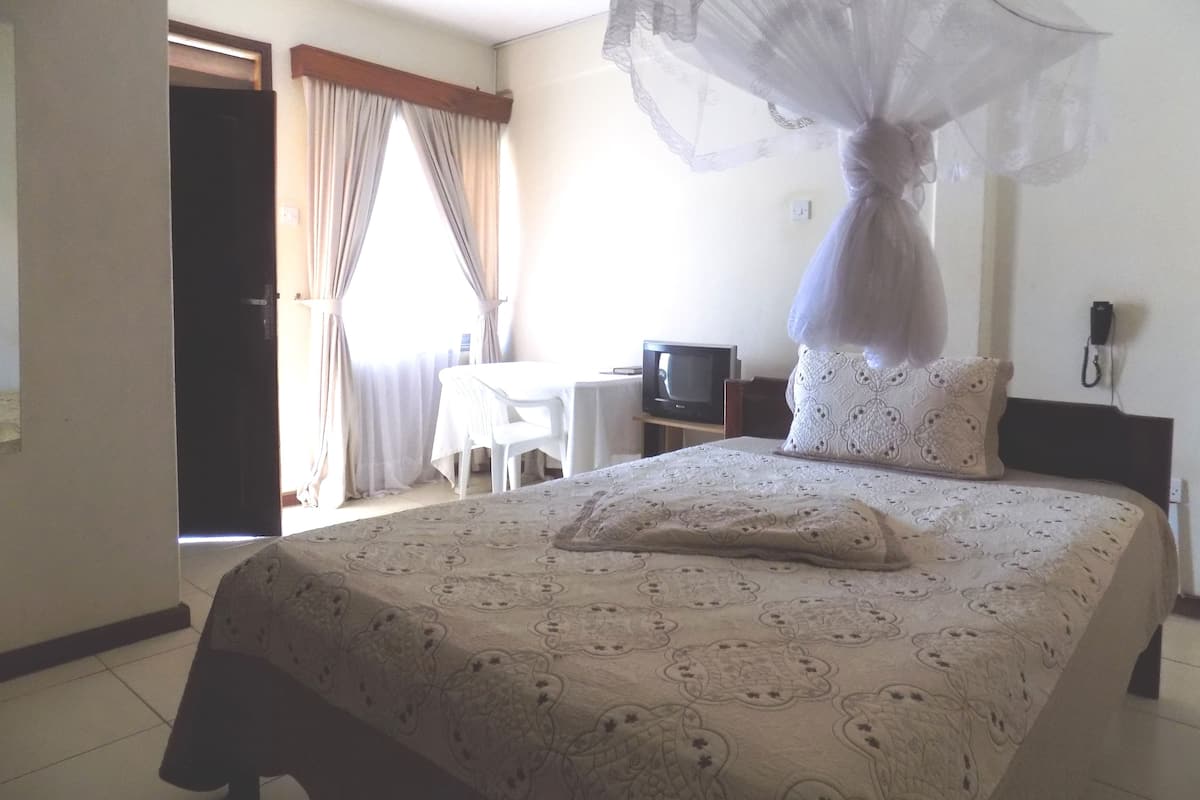 A hotel room with a bed, a TV, a desk, and a chair.