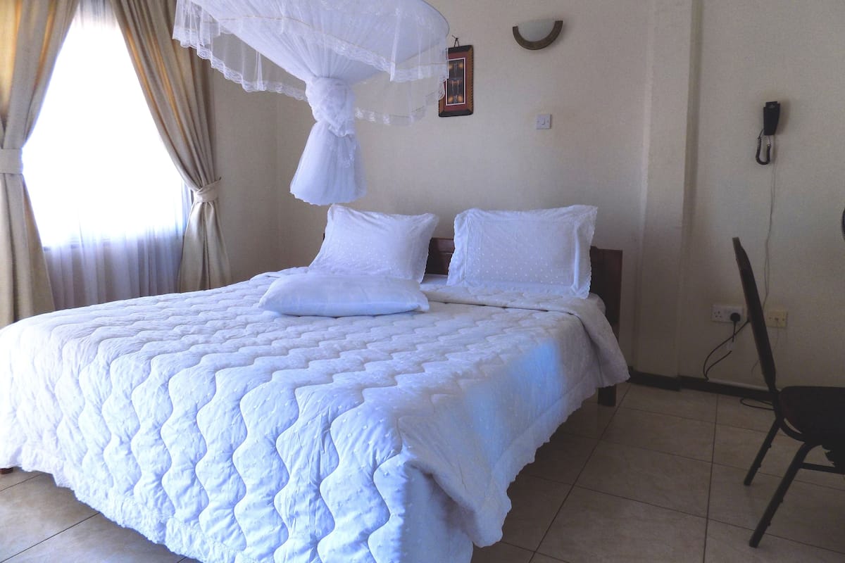 A neatly made bed with a white quilt, a white canopy, and a chair to the right.