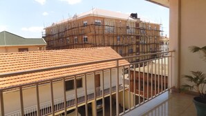 A building under construction with scaffolding, a tiled roof, and a balcony with a railing.