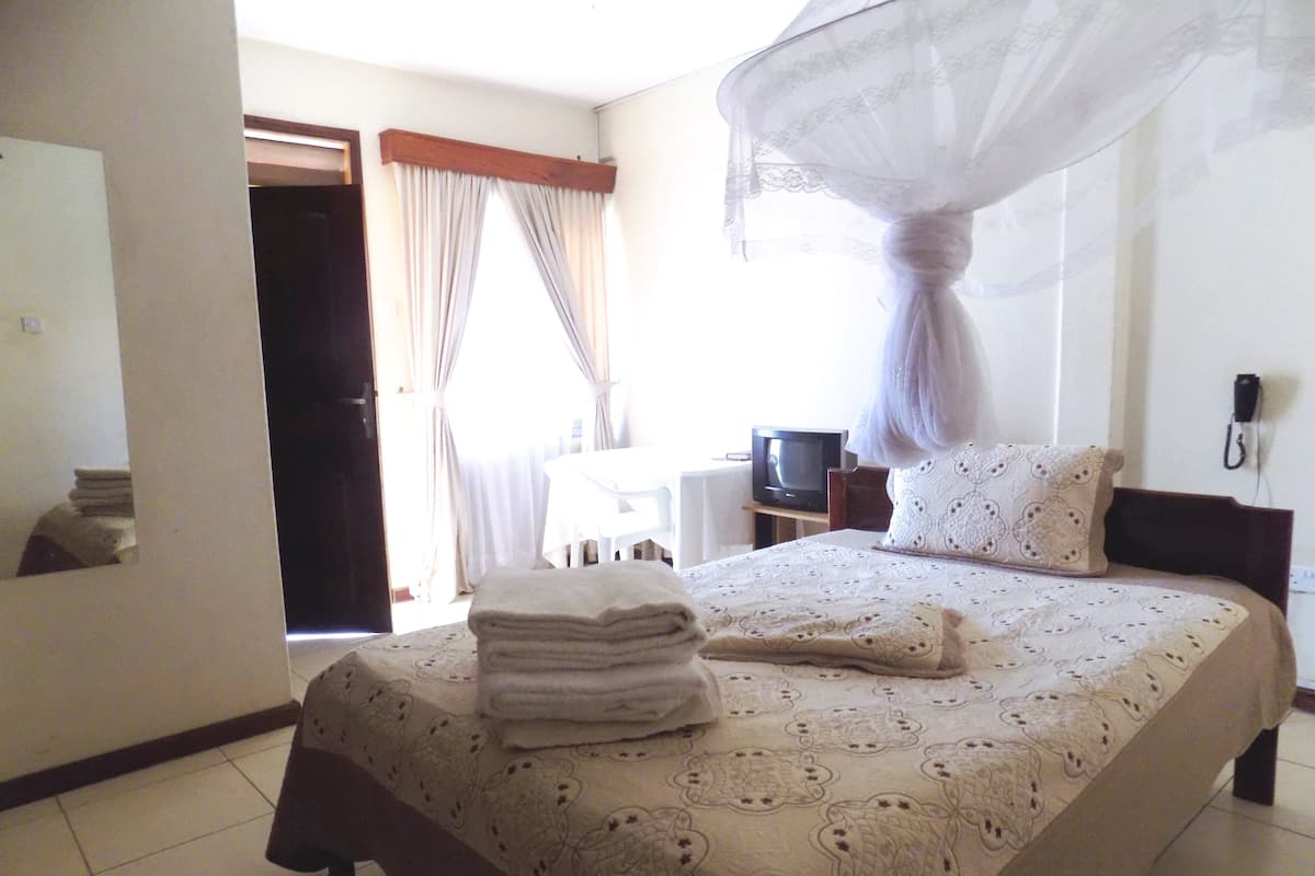 A hotel room with a bed, a TV, a bedside table, and a telephone.