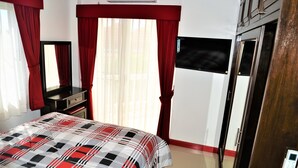 A hotel room with a bed, a TV, a wardrobe, and a mirror. - Luxury 1 bed Corner Condo (Pattaya)