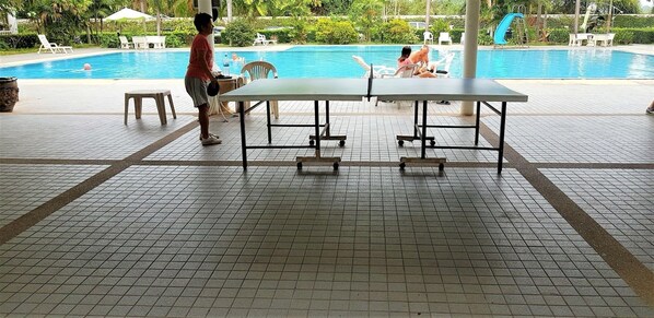 A poolside area with a table and chairs, a tiled floor, and a view of the pool.