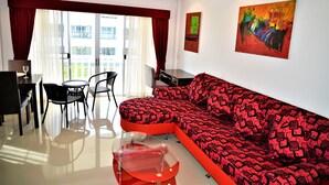 A modern living room with a red and black patterned sofa, a glass coffee table, and a dining area with chairs and a table. - Luxury 1 bed Corner Condo (Pattaya)