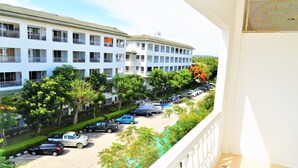 A multi-story building with balconies, a parking lot with several cars, and trees in the foreground. - Luxury 1 bed Corner Condo (Pattaya)