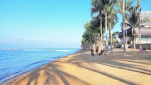 A beach with palm trees, a sandy shore, and a building with a sign in a foreign language. - Lovely Jomtien Beach Apartment (Pattaya)