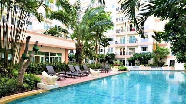 A swimming pool with lounge chairs and palm trees, surrounded by a multi-story building with balconies. - Park Lane Resort Jomtien Beach (Pattaya)