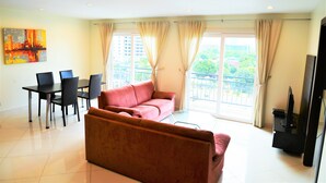 A living room with a red sofa, a dining table with chairs, a flat-screen TV, and large windows with curtains. - Park Lane Resort Jomtien Beach (Pattaya)