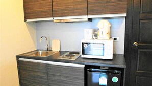 Een compacte keuken met donkerhouten kastjes, een roestvrijstalen spoelbak, een magnetron en een zwarte koelkast.