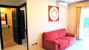 Een moderne woonkamer met een rode bank, een glazen salontafel en een wandairconditioner.