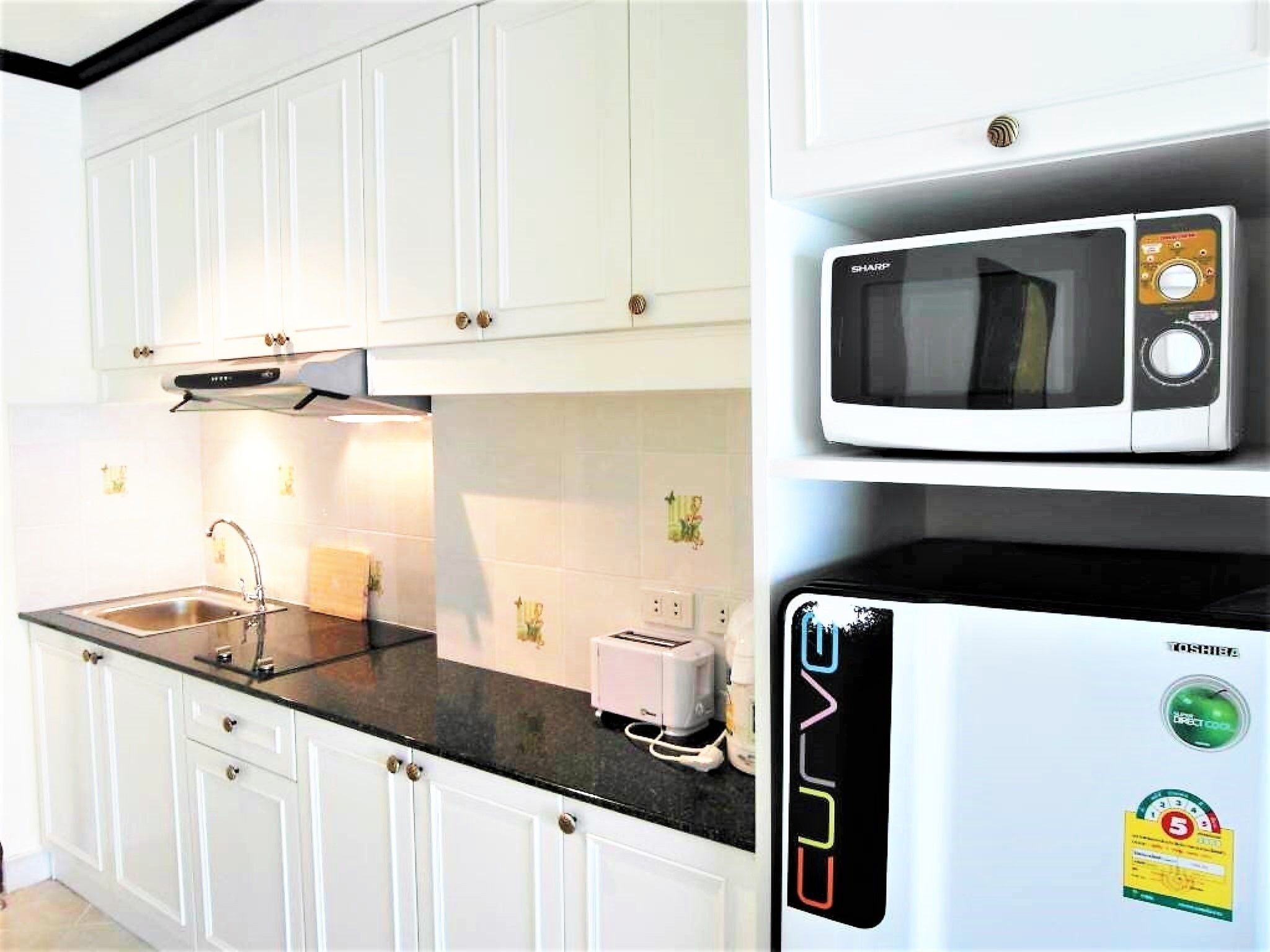 A kitchen with white cabinets, a black countertop, a microwave, and a refrigerator.