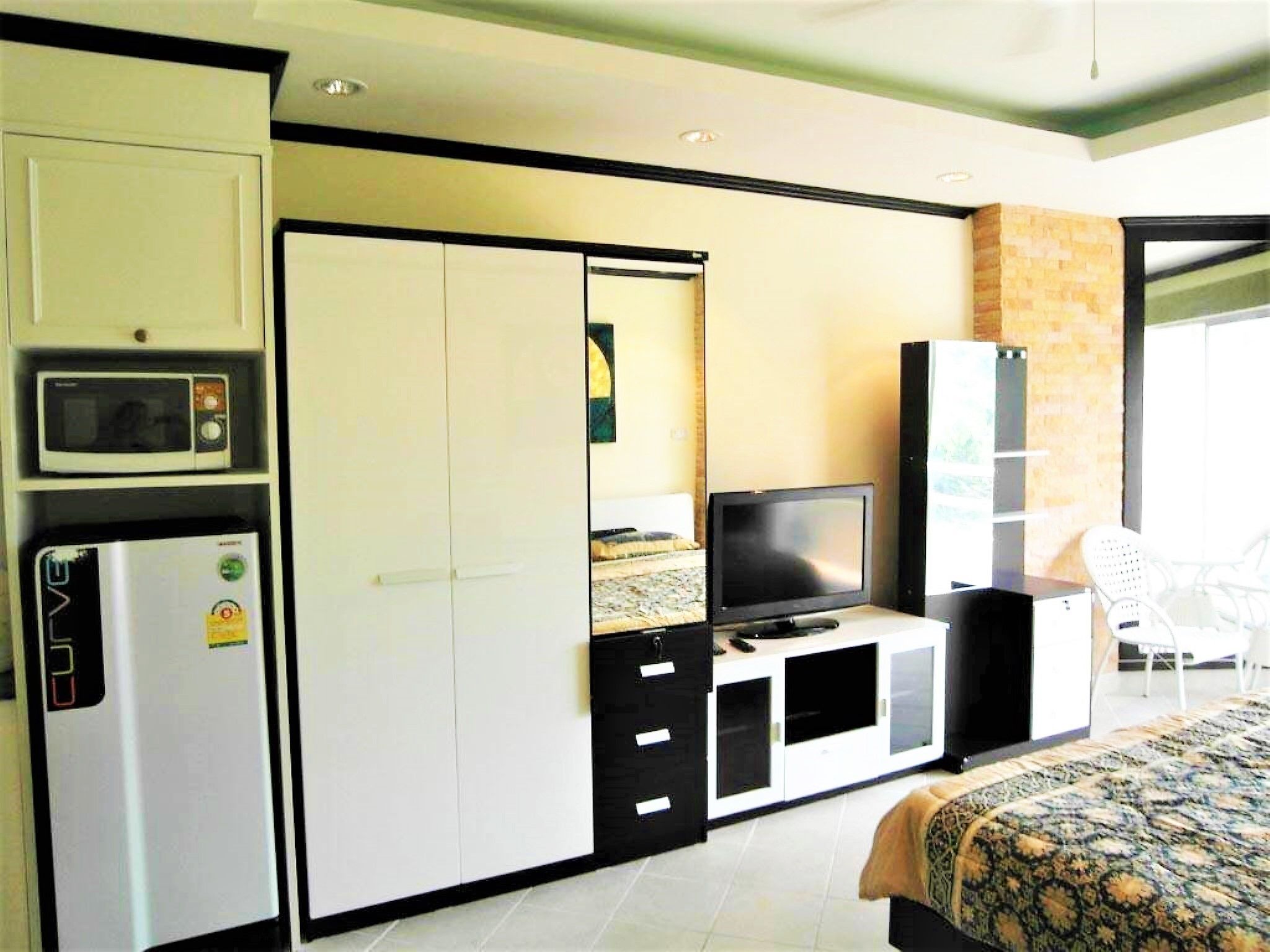 A hotel room with a bed, a TV, a microwave, a refrigerator, and a wardrobe.