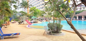 Un espace aménagé au bord de la piscine, avec des chaises longues, un toboggan et des palmiers.