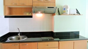 A kitchen with wooden cabinets, a stainless steel sink, a black countertop, and a range hood. - Lovely Studio at View Talay 1 (Pattaya)