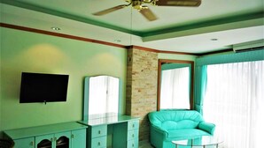 A room with a teal sofa, a glass coffee table, a flat-screen TV, a mirrored cabinet, and a ceiling fan. - Lovely Studio at View Talay 1 (Pattaya)