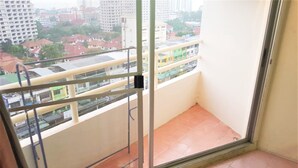 A balcony with a metal railing, a sliding glass door, and a view of a cityscape with buildings and a bridge. - Sea View Studio Jomtien (Pattaya)