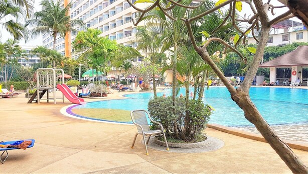 A poolside area with lounge chairs, a slide, and palm trees. - Sea View Studio Jomtien (Pattaya)