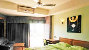 A hotel room with a bed, a chair, a desk, and a ceiling fan.