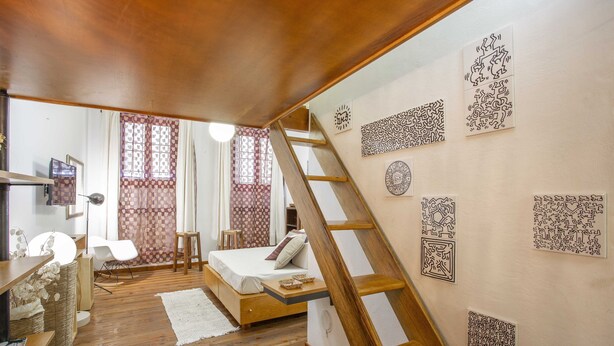 A bedroom with a wooden floor, a bed, a ladder, and decorative wall art.