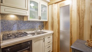 A kitchen with white cabinets, a gas stove, a sink, and a wooden door with a screen.
