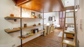 A room with wooden floors, a loft bed, a ladder, and shelves with various items.