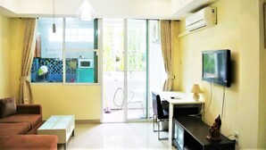Una sala de estar con un sofá, una mesa de centro, un televisor y un puerta corrediza de vidrio que da a un balcón.