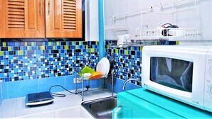 Una cocina con armarios de madera, salpicadero de azulejos, escurreplatos, microondas y una balanza.