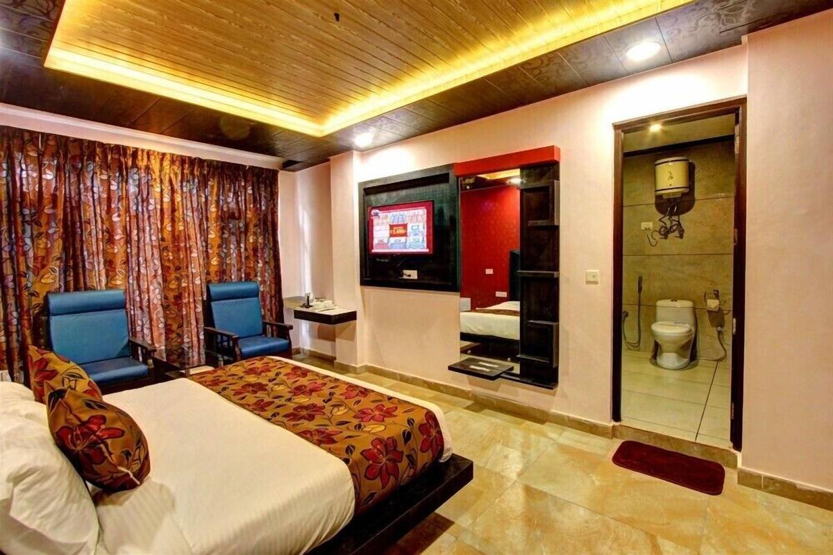 Ein Hotelzimmer mit einem Bett, zwei blauen Stühlen, einem Fernseher, einer Dusche und einem WC.