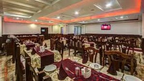 A banquet hall with rows of tables and chairs, a stage at the front, and a red ceiling light.
