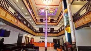 A hotel lobby with a central staircase, seating areas, and a reception desk.