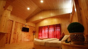 A wooden room with a bed, a small table, and a potted plant.