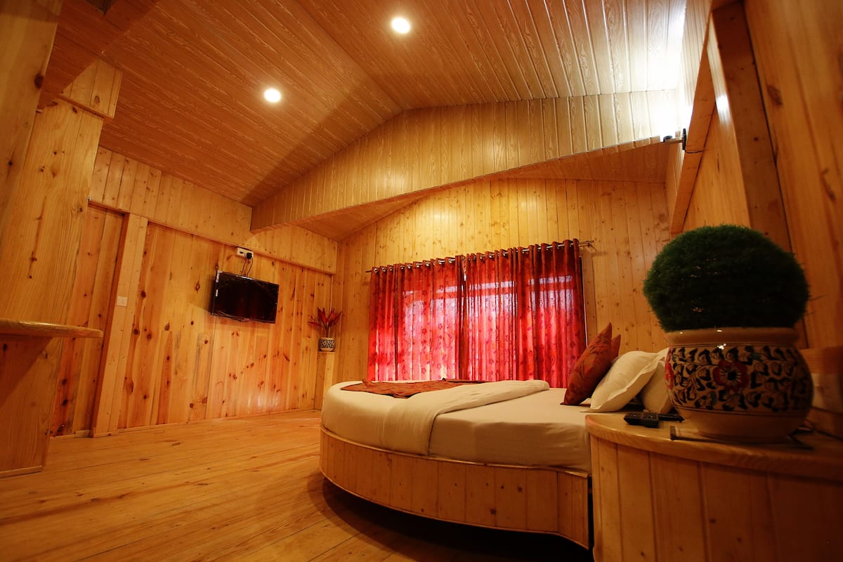 Ein Zimmer aus Holz mit einem Bett, einem kleinen Tisch und einer Topfpflanze.