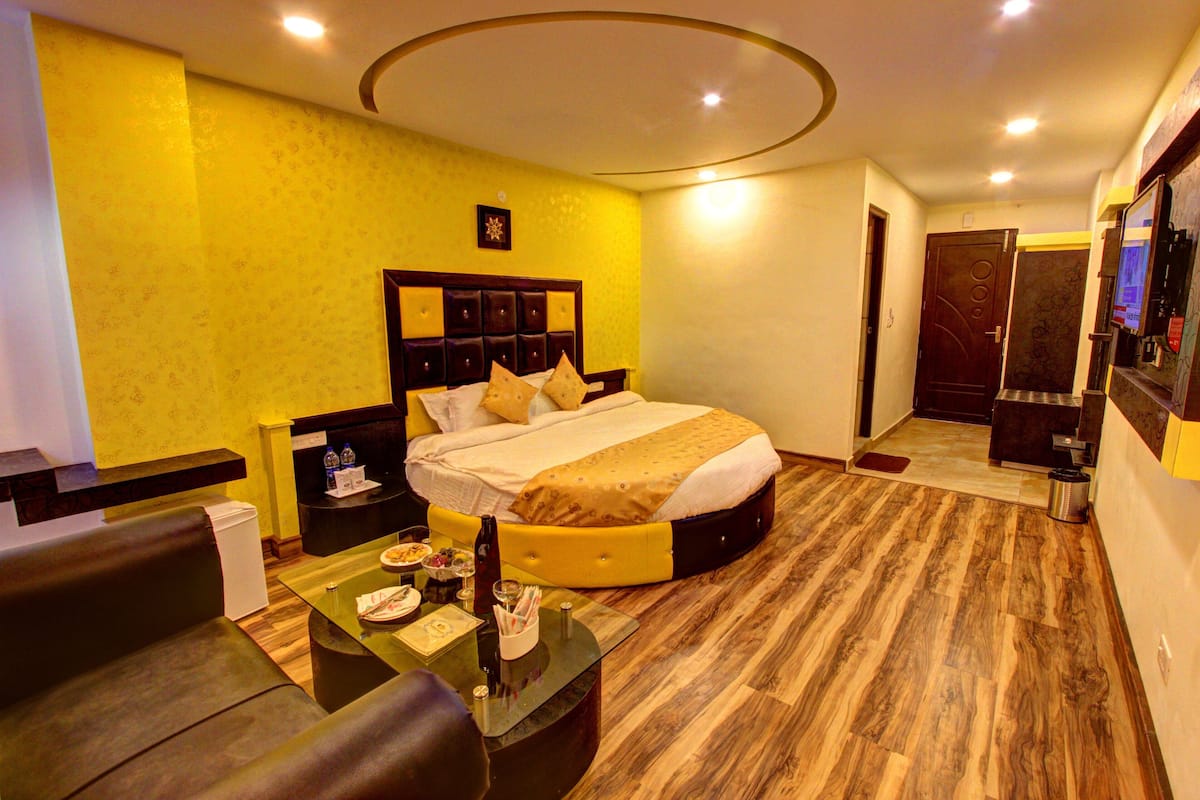 Ein Hotelzimmer mit einem großen Bett, einem kleinen Tisch mit Glasplatte, einer Couch und einer Minibar.