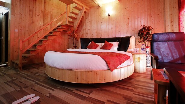 A wooden cabin interior with a circular bed, a staircase, a seating area, and a small table.