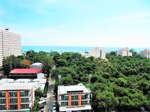 A multi-story hotel with a central courtyard, surrounded by dense greenery and a view of the sea.