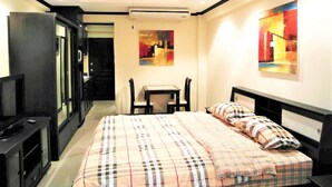 A hotel room with a bed, a desk, a chair, a television, and artwork on the walls. - Sea View Condo - Jomtien Beach (Pattaya)
