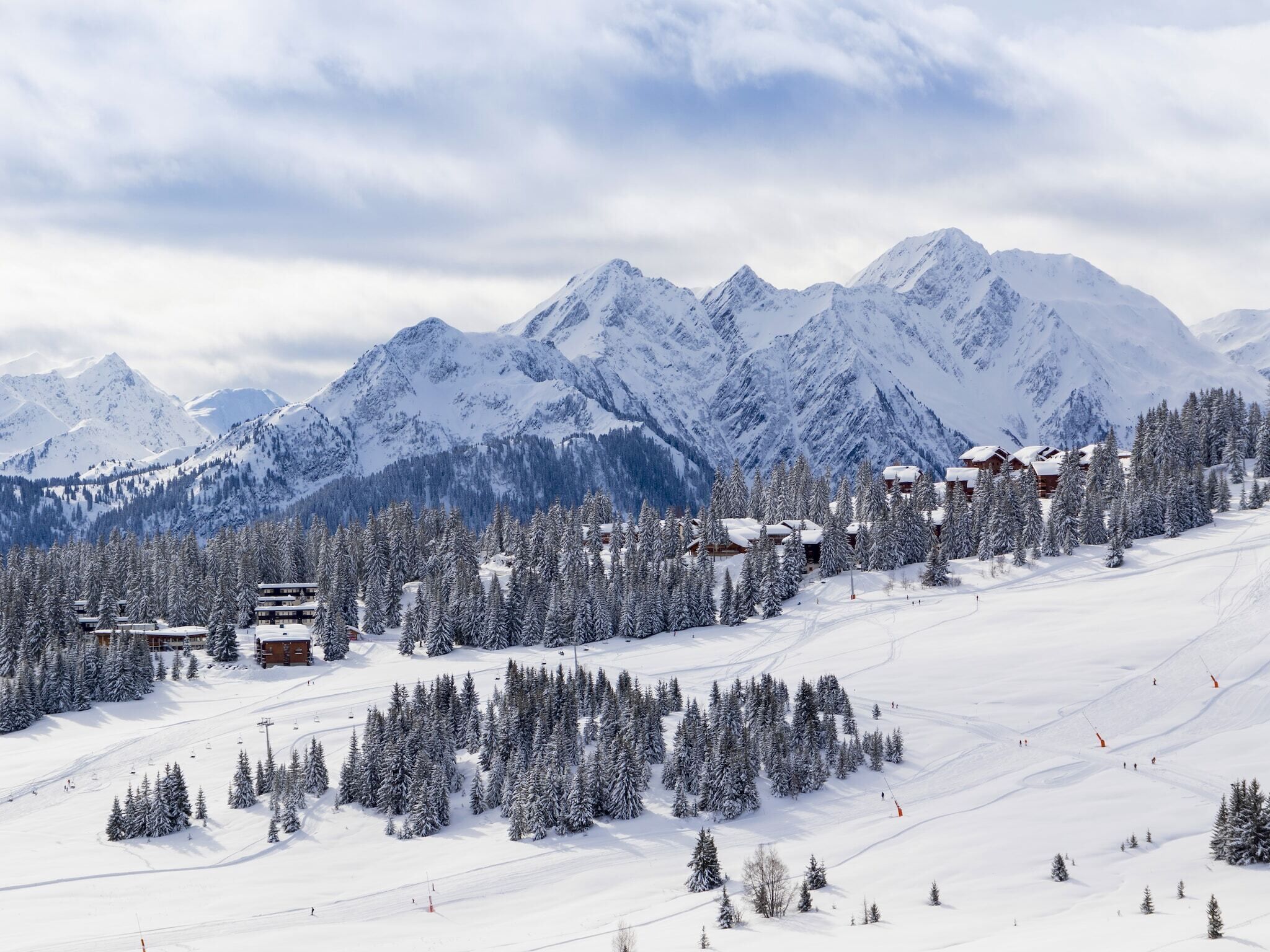Un complejo turístico en la montaña cubierto de nieve, con varias edificaciones de estilo chalet, pistas de esquí y montañas nevadas al fondo.