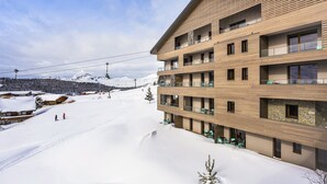 Un hotel de varios pisos con balcones, una pista de esquí al fondo y un paisaje nevado.