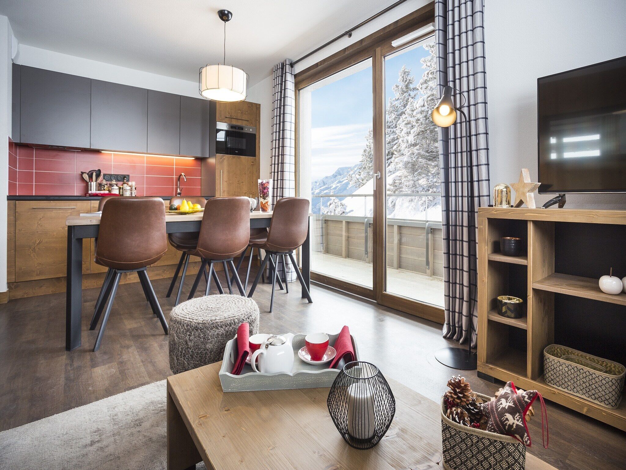 A modern kitchen with a dining area, large windows, and a TV.